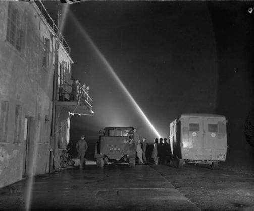Royal Air Force Bomber Command, 1942-1945. The Station Commander at Snaith, Yorkshire, Group Captain N H Fresson, is joined by other officers on the balcony of the control tower as they await the return of Handley Page Halifaxes of No. 51 Squadron RAF from a night raid on Nuremberg. Note the ambulance and crash tenders with their crews standing by below the tower, and the searchlight beam pointing skywards to show the cloud base. Five aircraft failed to return to Snaith on this night, and a sixth crashed on landing. Copyright: xpiemagsx airministryww2pie13032022-1753 !ACHTUNG AUFNAHMEDATUM GESCHÄTZT!