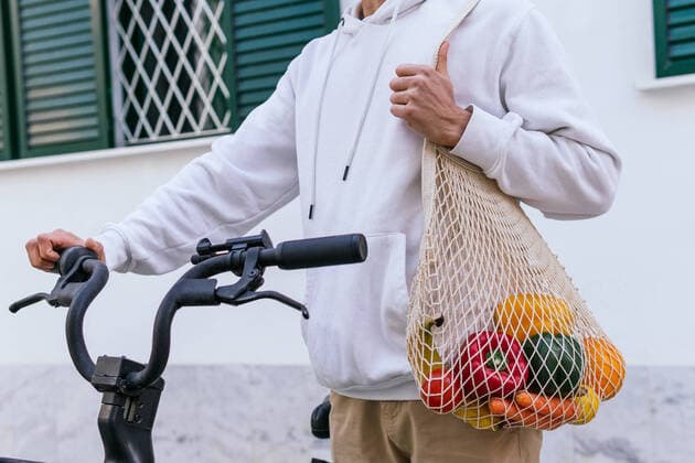 IMAGO Creative: St?dte im Wandel Crop unrecognizable male with groceries in eco friendly mesh bag standing near modern bike in city street, Model released DavidMunoz_AlejandroEco_35 Copyright: xDavidxMunozx MR