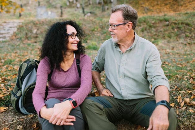 IMAGO Creative: Welttag f?r psychische Gesundheit am 10. Oktober Cheerful mature couple in casual wear sitting looking at each other on the ground in autumn park, Model released Lightsy_HikingSeniors_15 Copyright: xLightsyx MR