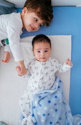 From above of charming happy little boy holding hands of little baby sibling while lying down peacefully together in cozy bed, Model released NehomarHernandez_HomeKidGames_12 Copyright: xNehomarxHernandezx MR