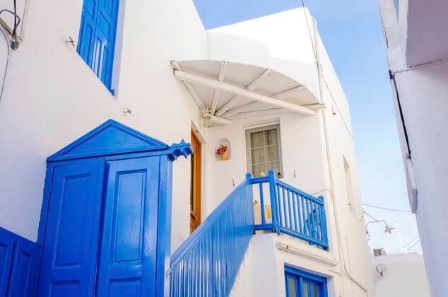 A very traditional alley view of the architecture in Chora, on the greek island Mykonos, Greece. A blue door, fence and windows of a whitewashed house against the blue sky. , 21668310.jpg, mykonos, greece, architecture, greek island, travel, greek, blue, alley, mikonos, myconos, chora, island, destination, summer, whitewashed, fence, picturesque, door, alleyway, traditional, tourist, frame, colourful, street, town, hora, stone, houses, winds, white, typical, landmark, attraction, holiday, sunny, aegean, sun, village, building, window, sightseeing, cosmopolitan, city, cyclades, tourism, mediterranean, vacation, capital, santorini, hellas,