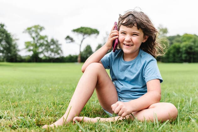 Creative Highlights Symbolbilder Full body of cheerful child in casual clothes barefoot and looking away while sitting on lawn and answering phone call on summer weekend day in park, Model released HodeiUnzueta_ID559_21856_049 Copyright: xHodeixUnzuetax MR