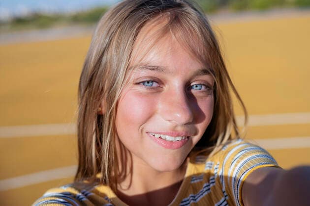 Creative Highlights Symbolbilder Happy teenage girl looking at camera with smile while taking self portrait on sunny street against blurred sports ground background on summer day, Model released JoseLuisCarrascosa_ID441_16855_031 Copyright: xJosexLuisxCarrascosax MR