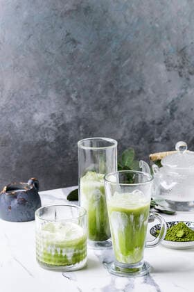 Matcha iced latte Matcha green tea iced latte or cocktail in three different glasses with ice cubes, matcha powder and jug of milk on white marble table, decorated by green branches. Grey wall at background Copyright: xNatashaxBreenx NB100718-69
