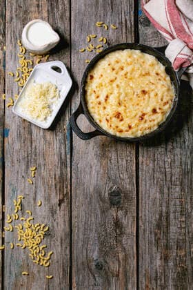 American dish mac and cheese Classic american dish baked mac and cheese in cast iron pan with kitchen towel and ingredients above over old wooden background. Flat lay, space Copyright: xNatashaxBreenx NB160919-17