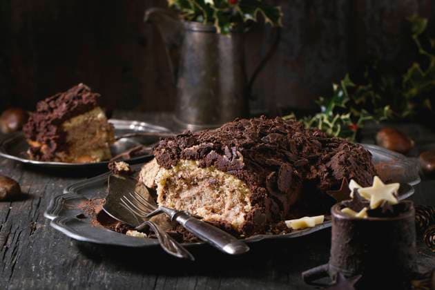 Sliced christmas chocolate yule log Sliced homemade Christmas chocolate yule log with chestnuts cream on vintage plate with forks, chocolate stars and holly branch over old wooden table. Dark rustic style. Copyright: xNatashaxBreenx NB271016-7