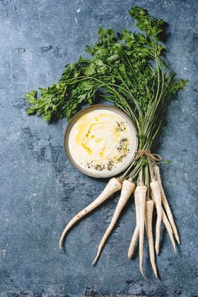 Parsnip soup with butter sauce Parsnip cream soup in ceramic bowl with butter sauce, bundle of fresh parsnip and herbs over blue texture background. Flat lay, space Copyright: xNatashaxBreenx NB300919-3