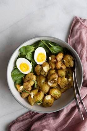 Smashed roasted potatoes in a salad bowl with baby spinach and hard boiled eggs with spoons photographed on a light marble background. Copyright: xYusufxRizaxGunaydinx YG230520-19