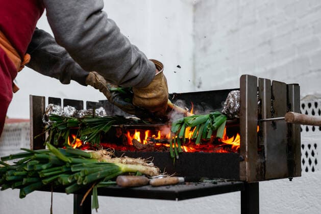 Crop anonymous person in protective gloves grilling traditional Catalonian calcots on hot barbecue grid with foil while standing on terrace, Model released AidaMartinez_BBQCalcots_11 Copyright: xAidaxMartinezx MR