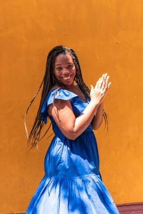 Creative Highlights Symbolbilder Side view of content African American female with braids and in dress clapping hands on yellow background in city on sunny day and looking at camera, Model released HectorPertuz_MultiethnicCouple_38 Copyright: xHectorxPertuzx MR