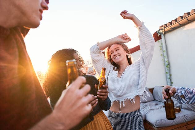 IMAGO Creative, Urban Lifestyle IMAGO Kreativ: Urbane Kultur - Sommer auf den D?chern Group of joyful young multiracial friends wearing casual clothes enjoying cold beer and dancing with arms raised together on rooftop at sunset, Model released, Property released ManuelRuiz_FlatmatesMusiciansTerrace_68 Copyright: xManuelxRuizx MR