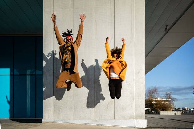 IMAGO Creative: Herbst in der Stadt Vividly dressed black woman and man in coat jumping with arms raised above street in bright sunlight, Model released RafaCortes_AlphaDayanis_57 Copyright: xRafaxCortesx MR