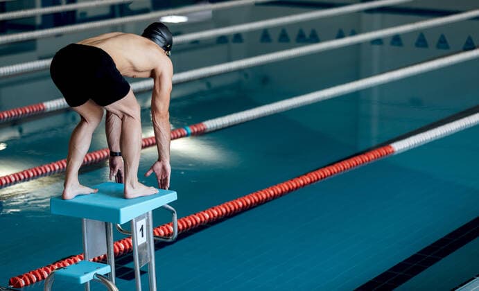 Back view of anonymous male athlete in swimming trunks leaning forward on starting platform over pool with floating markers, Model released SergioVictorVega_MaiquelSwimmer_7 Copyright: xSergioxVictorxVegax MR