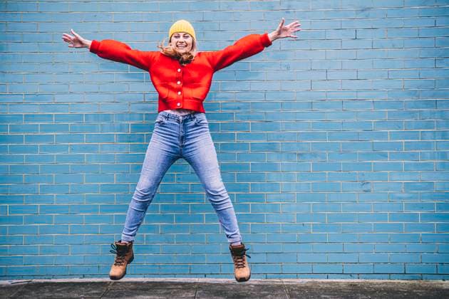 Carefree young woman jumping with arms outstretched in front of wall model released, Symbolfoto, AMWF00316