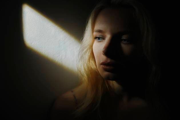 Sad young woman sitting in front of wall by rays of sunlight model released, Symbolfoto, AZF00433
