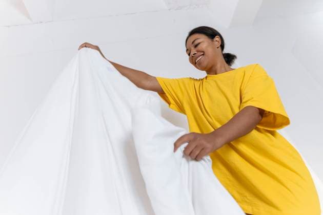 IMAGO Creative: Frühjahrsputz Young woman in yellow t-shirt smoothes the duvet in the bedroom model released, Symbolfoto property released, SIF00398