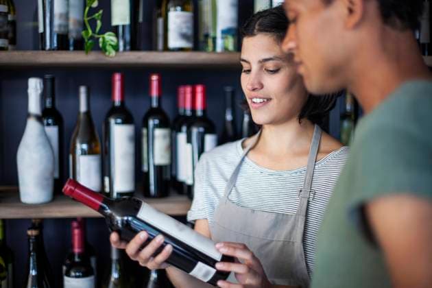 RECORD DATE NOT STATED Wine store coworkers reading wine bottle label while standing indoors Copyright: DinocoxGreco B64331741