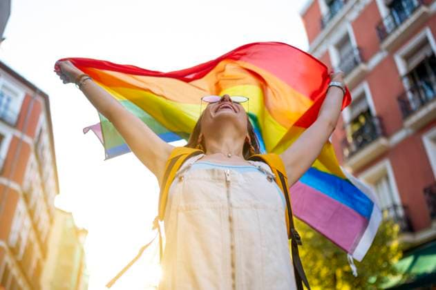 From below cheerful young female in crop top and sunglasses smiling and holding transgender flag behind back on sunny summer day on street JoseLuisCarrascosa_ID768_28605_032 Copyright: xJosexLuisxCarrascosax Model Released