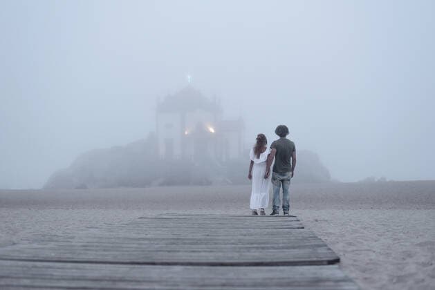 Back view of unrecognizable couple of travelers holding hands on sandy seashore against Chapel of Senhor da Pedra in Vila Nova de Gaia in Porto Portugal, Model released FranciscoCarrodeguas_CentralPortugal_54 Copyright: xFranciscoxCarrodeguasx MR