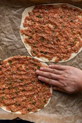 Woman making lahmacun from scratch with homemade dough and ground beef filling on a parchment paper lined baking sheet. Copyright: xYusufxRizaxGunaydinx YG100720-8