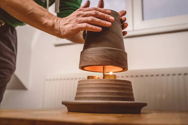 30 September 2022: young man warming his hands on a tealight heater to save electricity and gas. homemade tealight stove, DIY heater from plant pot and tealight candles *** junger Mann wärmt sich die Hände an einer Teelichtheizung um Strom und Gas zu sparen. selbstgebauter Teelicht Ofen, DIY Heizung aus Pflanzentopf und Teelicht Kerzen
