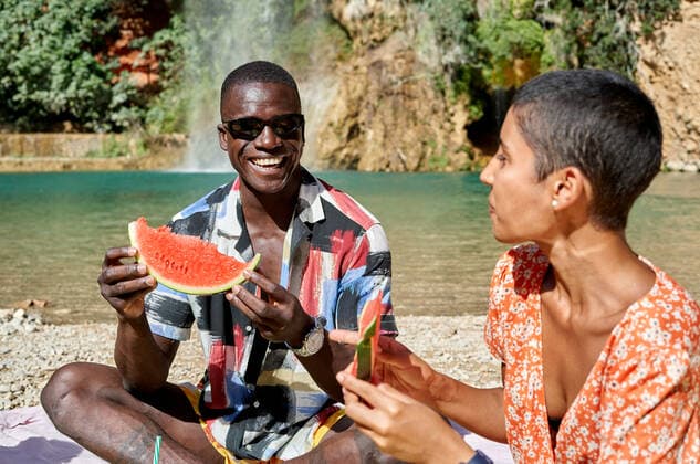 Multiracial cheerful couple sitting together and eating watermelon while having picnic against lake in summer, Model released, Property released AdalbertoRodriguez_ID942_34991_020 Copyright: xAdalbertoxRodriguezx MR