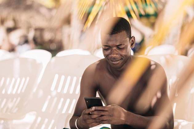 IMAGO Creative: November, Monat der Männergesundheit Glad black man using smartphone on beach Bayahibe, La Altagracia Province, Dominican Republic CR_JURA221024-1049696-01 ,model released, Symbolfoto