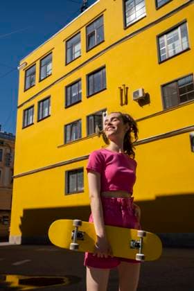 IMAGO Creative, Jahreszeit Sommer, Sommer in der Stadt Woman with skateboard standing in front of building on sunny day model released, Symbolfoto, VPIF07374