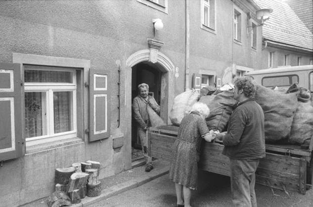 DDR, Sachsen, historisch, Wirtschaft, Volkswirtschaft, Betriebe (VEB Volkseigene Betriebe): Dresdner Kohlehandel, Betriebsteil Pirna, Arbeitsalltag, Anlieferung beim Kunden Privathaushalt, Abladen von Kohlesäcken vom W50, Arbeiter und Kundin Mieterin namentlich nicht benannt. August 1987. Veröffentlichung in Sächsische Zeitung am 21.08.1987: Der nächste Winter kommt sicher. Einer der fünf Betriebsteile des Dresdner Kohlehandels ist der in Pirna. Hier kommt an jedem Tag ein Güterzug des Braunkohlenkombinats Schwarze Pumpe an, aus dem bis zu 600 Tonnen Briketts und 200 Tonnen Klarkohle entladen werden müssen. Insgesamt sind es 1.100 Tonnen, die von den über 100 Kohlearbeitern mit Groß- und Kleinfahrzeugen, vom Skoda, W 5O, Robu Copyright: xSZ GunterxHübnerx 0000010121133590 ! ACHTUNG Aufnahmedatum laut Beschriftung