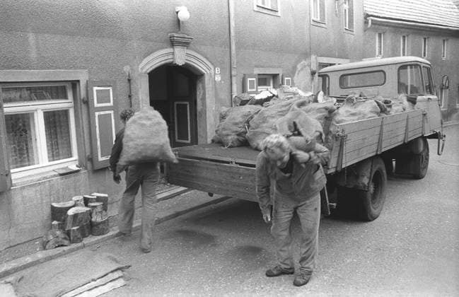 DDR, Sachsen, historisch, Wirtschaft, Volkswirtschaft, Betriebe (VEB Volkseigene Betriebe): Dresdner Kohlehandel, Betriebsteil Pirna, Arbeitsalltag, Anlieferung beim Kunden Privathaushalt, Abladen von Kohlesäcken vom W50, Arbeiter namentlich nicht benannt. August 1987. Veröffentlichung in Sächsische Zeitung am 21.08.1987: Der nächste Winter kommt sicher. Einer der fünf Betriebsteile des Dresdner Kohlehandels ist der in Pirna. Hier kommt an jedem Tag ein Güterzug des Braunkohlenkombinats Schwarze Pumpe an, aus dem bis zu 600 Tonnen Briketts und 200 Tonnen Klarkohle entladen werden müssen. Insgesamt sind es 1.100 Tonnen, die von den über 100 Kohlearbeitern mit Groß- und Kleinfahrzeugen, vom Skoda, W 5O, Robur bis zum Multicar verte Copyright: xSZ GunterxHübnerx 0000010121133598 ! ACHTUNG Aufnahmedatum laut Beschriftung