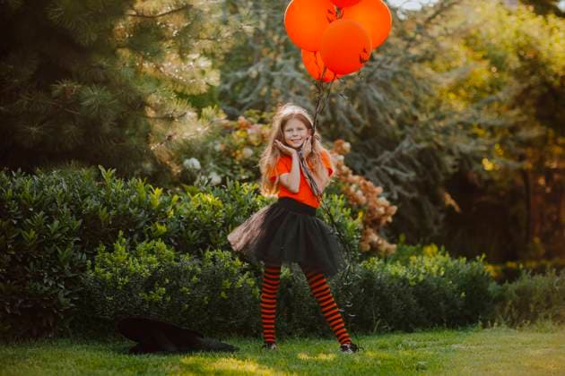 Smiling girl holding orange balloons standing with head in hands at back yard model released, Symbolfoto, MDOF00104