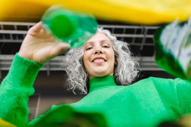 Smiling woman with gray hair putting green bottle in yellow plastic bag model released, Symbolfoto, SEAF01479