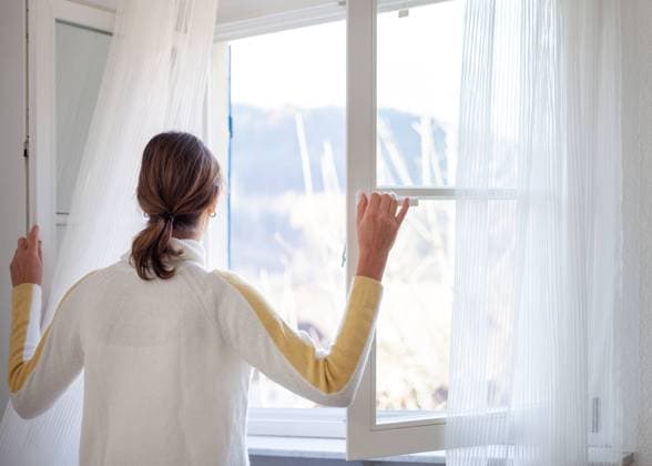 Lüften der Wohnung - Frau steht am Fenster und öffnet es weit mit Blick nach draußen, model released - Deutschland *** Airing the apartment woman stands at the window and opens it wide with view outside, model released Germany