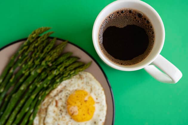 From above breakfast dish of fried egg with green asparagus server on plate next to cup of coffee on yellow background MaryMiro_ID3343_109454_002 Copyright: xMaryxMirox Model Released
