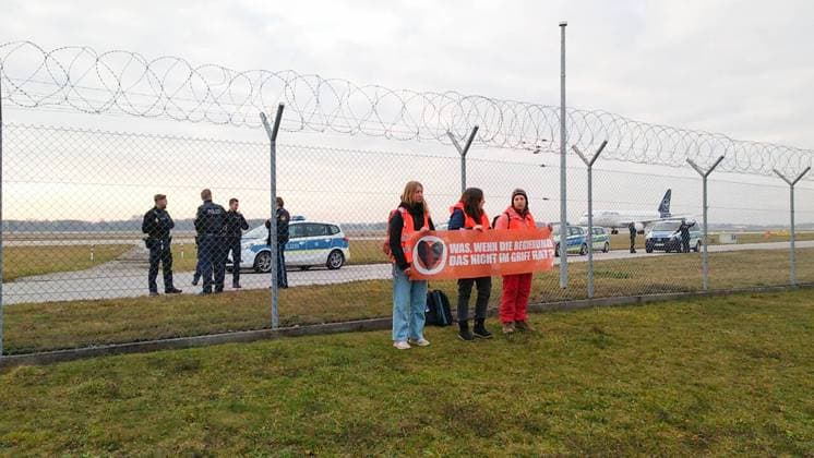 Letzte Generation demonstriert am Flughafen München Aktivist*innen der Letzten Generation demonstrierten am 8.12.2022 vor dem Stcheldrahtzaun des Münchner Flughafens für die Wiedereinführung des Neun-Euro-Ticket und ein Tempolimit von 100 km h auf deutschen Autobahnen. -- Activists of the Last Generation demonstrated on December 8, 2022, in front of the barbed wire fence of Munich Airport for the reintroduction of the 9-euro ticket and a speed limit of 100 km h on German highways. Flughafen München Bayern Deutschland Copyright: xLGPBx