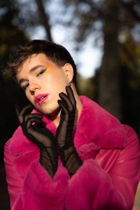 Creative Highlights Symbolbilder Androgynous young man with short hair and makeup in bright pink leather coat touching face with gloves while standing in path amidst trees in autumn forest on sunny day, Model released DanielPerezLozao_ID10613_321525_009 Copyright: xDanielxPerezxLozaox MR