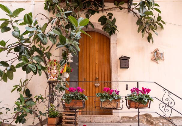 Exterior of residential building with wooden door decorated by potted blooming flowers and green plants located in Taormina JuanAlbertoRuiz_ID10562_320152_009 Copyright: xJuanxAlbertoxRuizx Model Released