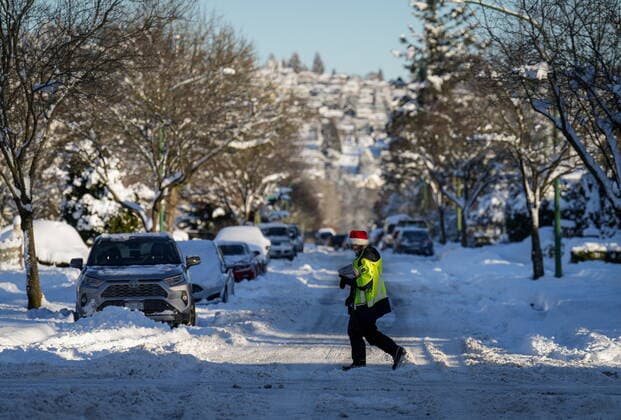 December 21, 2022, BURNABY, BC, CANADA: A Canada Post letter carrier crosses a snow and ice covered road while delivering mail in Burnaby, B.C., on Wednesday, December 21, 2022. A snowstorm dumped more than 30 centimetres of snow in Metro Vancouver this week. BURNABY CANADA  - ZUMAc35_ 20221221_zaf_c35_041 Copyright: xDarrylxDyckx