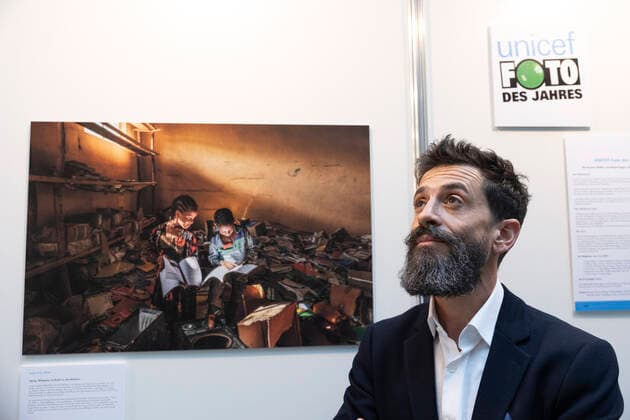 Photographer Eduardo Soteras on 22 12 2022 in front of the Unicef Photo of the Year 2022 in the exhibition at the Haus der Bundespressekonferenz in Berlin The Unicef Photo of the Year 2022 by renowned Argentine photographer Eduardo Soteras shows two children engrossed in books in the destroyed library of an elementary schoo Copyright: epd-bild HansxScherhaufer epd-UNICEF-Foto_2022-5-kopieren