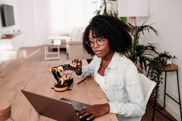 Engineer using laptop holding robot model at desk in home office model released, Symbolfoto property released, EBBF06987