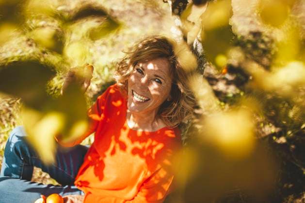 Happy mature woman sitting with orange fruits under tree model released, Symbolfoto property released, JOSEF15597