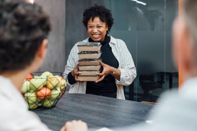 Cheerful young woman with lunch boxes standing by table in office model released, Symbolfoto property released, VPIF07749