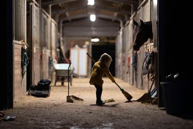 IMAGO Creative, Kinder auf dem Reiterhof Girl sweeping illuminated stable with broom model released, Symbolfoto property released, NJAF00093