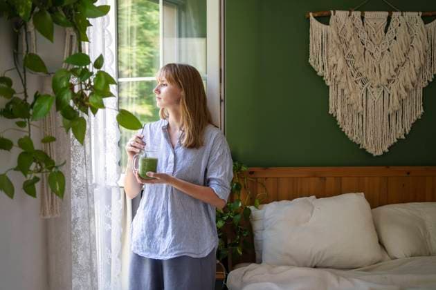 IMAGO Creative, Lifestyle, Tik Tok-Trend thatgirl Thoughtful woman with green smoothie standing by window model released, Symbolfoto property released, SVKF00952
