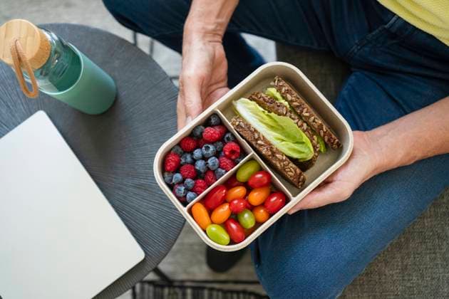 Hands of man holding lunch box with healthy food on sofa model released, Symbolfoto property released, SVKF01015