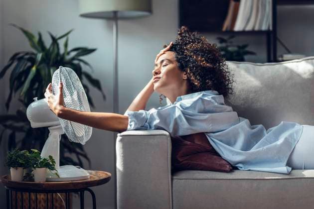 Young woman cooling off using electric fan lying on sofa at home model released, Symbolfoto property released, JSRF02352