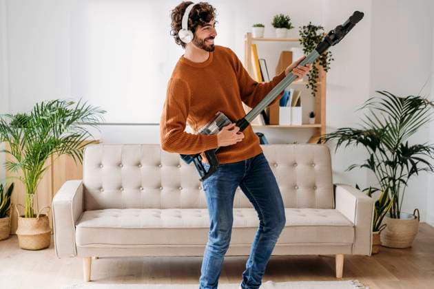 Happy young man dancing and playing guitar with vacuum cleaner at home model released, Symbolfoto property released, EBBF07487