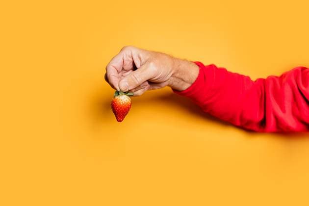 Crop hand of male demonstrating delicious ripe strawberry on yellow background in studio, Model released HodeiUnzueta_ID12584_382495_015 Copyright: xHodeixUnzuetax MR