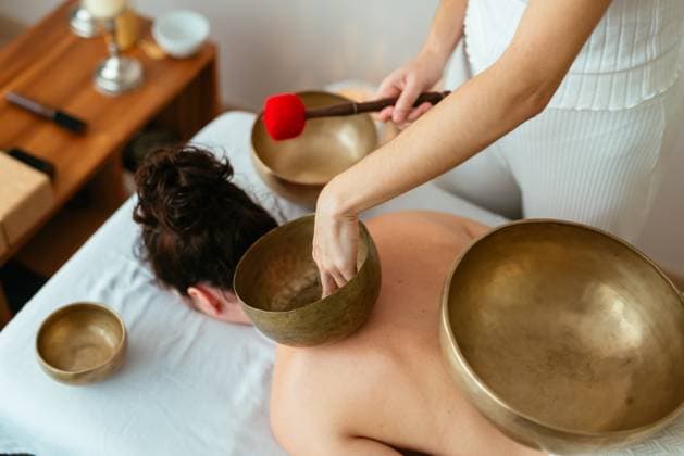 From above of crop unrecognizable woman playing Tibetan bowl of various sizes while performing meditating song for anonymous female client lying on table during session AidaMartinez_ID12552_381093_049 Copyright: xAidaxMartinezx Model Released
