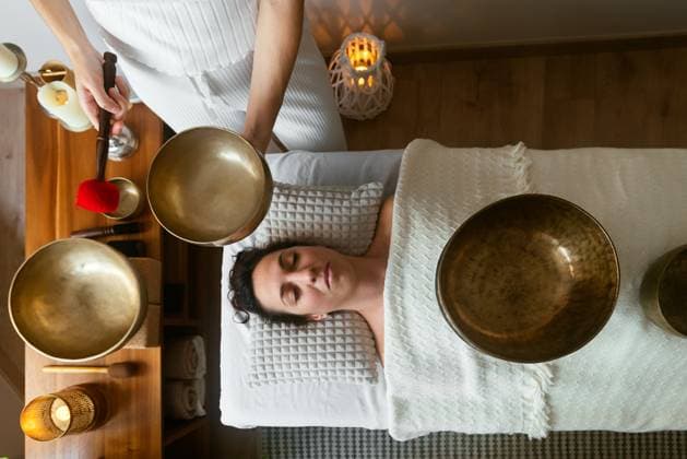 Top view of relaxed young ethnic female client lying on massage table with closed eyes while therapist playing traditional Tibetan singing bowl during meditation session in spa salon AidaMartinez_ID12552_381101_056 Copyright: xAidaxMartinezx Model Released